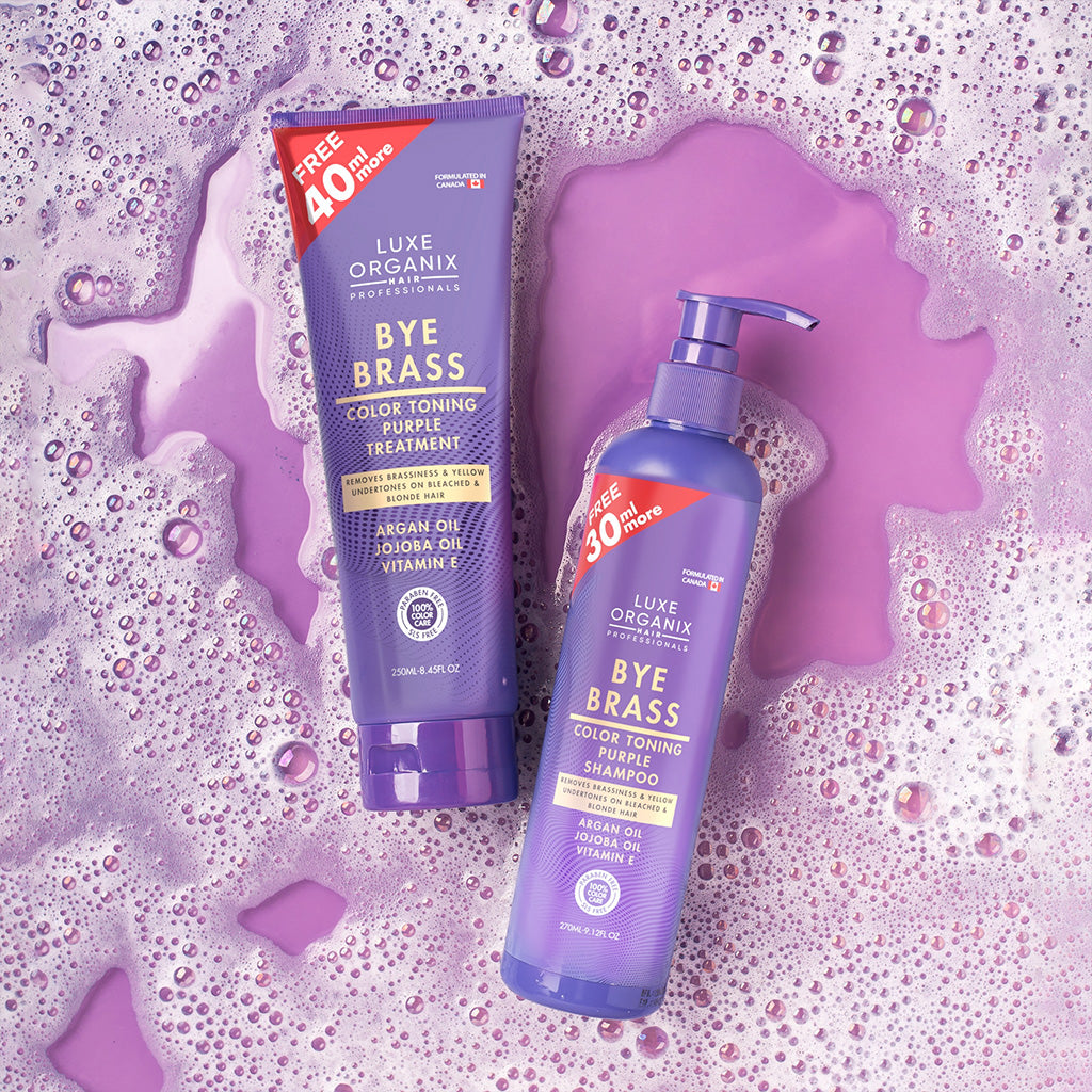 Luxe Organix Bye Brass shampoo and treatment on a purple background with soap suds.